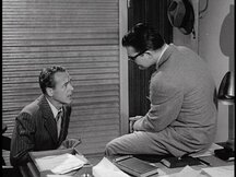 In Clark's office, Hadley talks to Clark as Clark sits on the desk